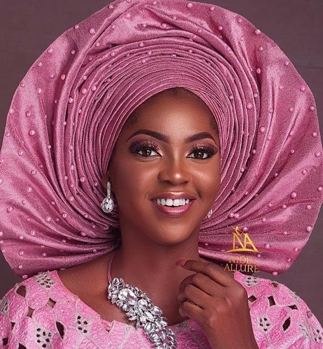 Portrait of a Nigerian woman wearing a sculptural gele headwrap at a wedding celebration