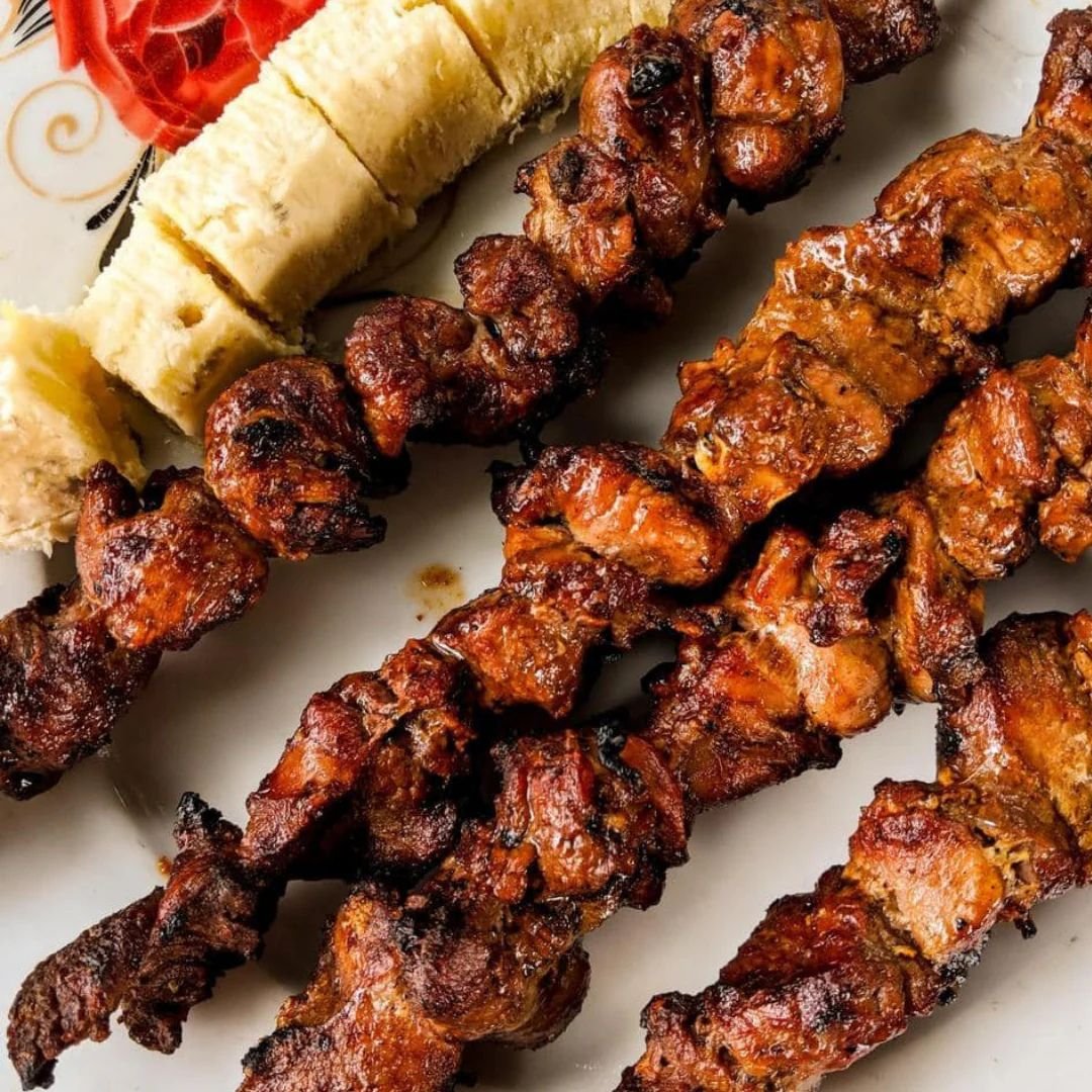 Rwandan brochette skewers served with fried plantains and roasted meat on white plate