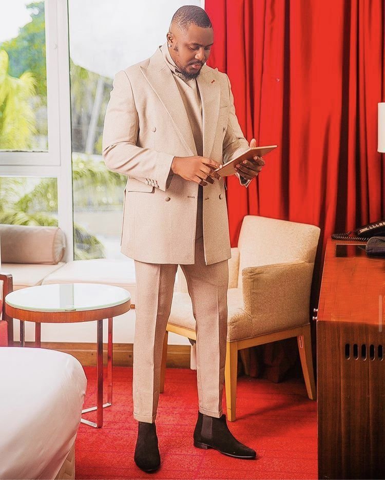 Well dressed African man in beige double-breasted suit standing indoors holding a tablet